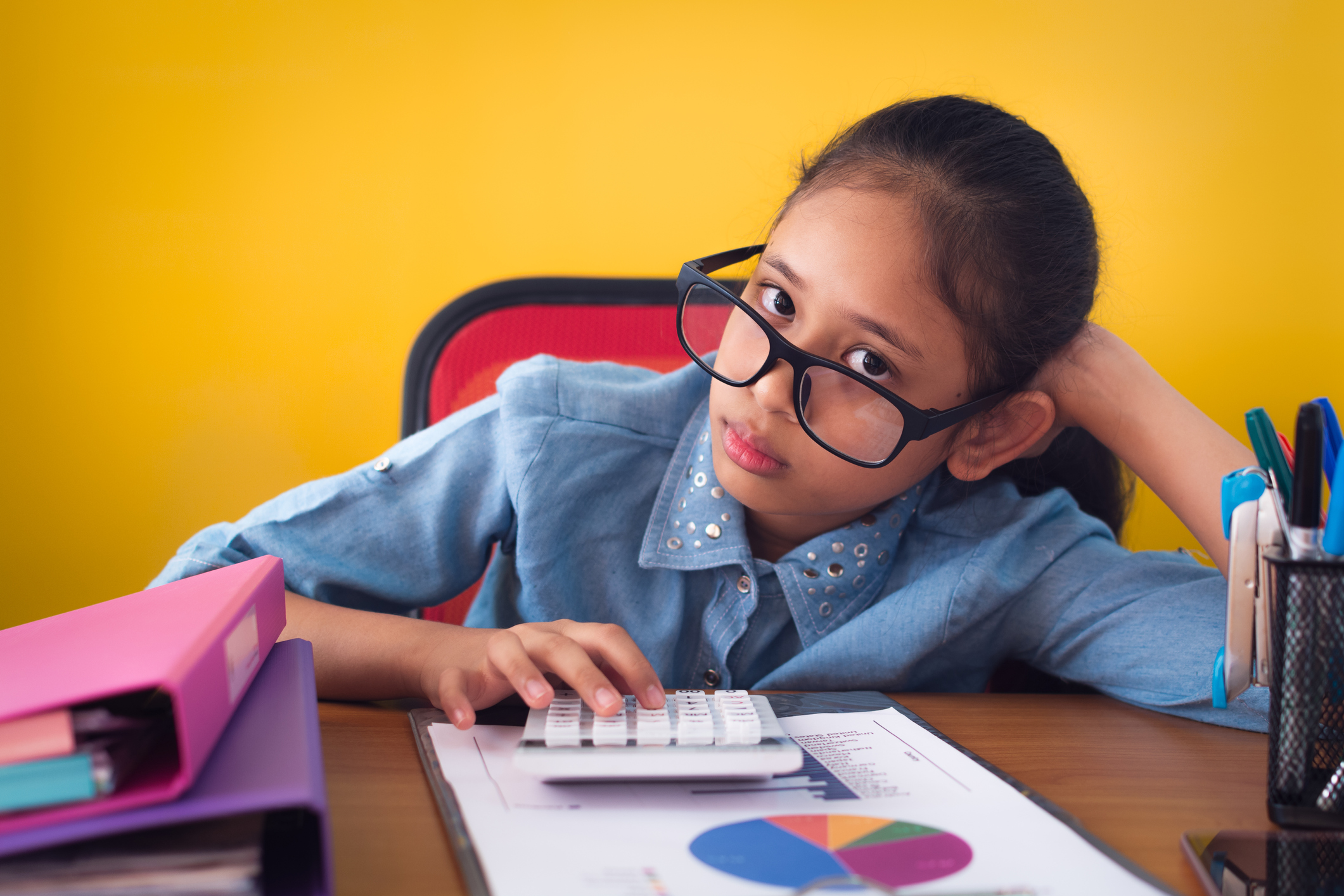 Cute girl wearing glasses is boring with hard work on the desk isolated on yellow background.