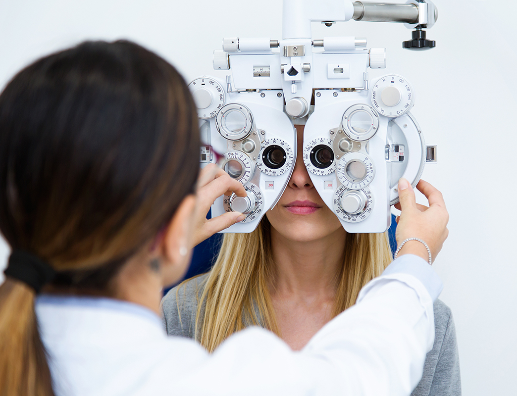 Young woman sitting on chair with beautiful optician standing while doing eye test in ophthalmology clinic.