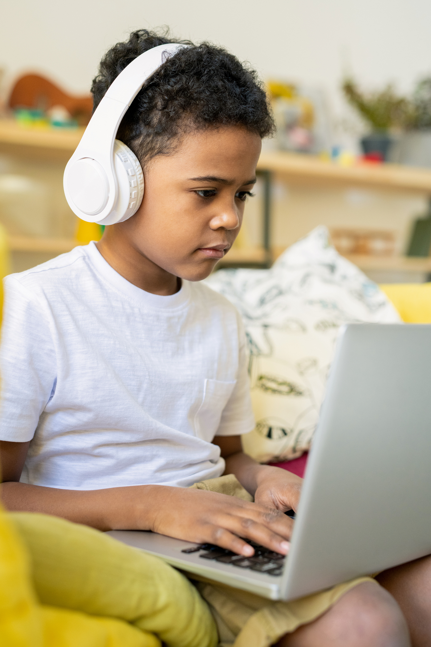 Elementary schoolboy of African ethnicity with headphones typing on laptop