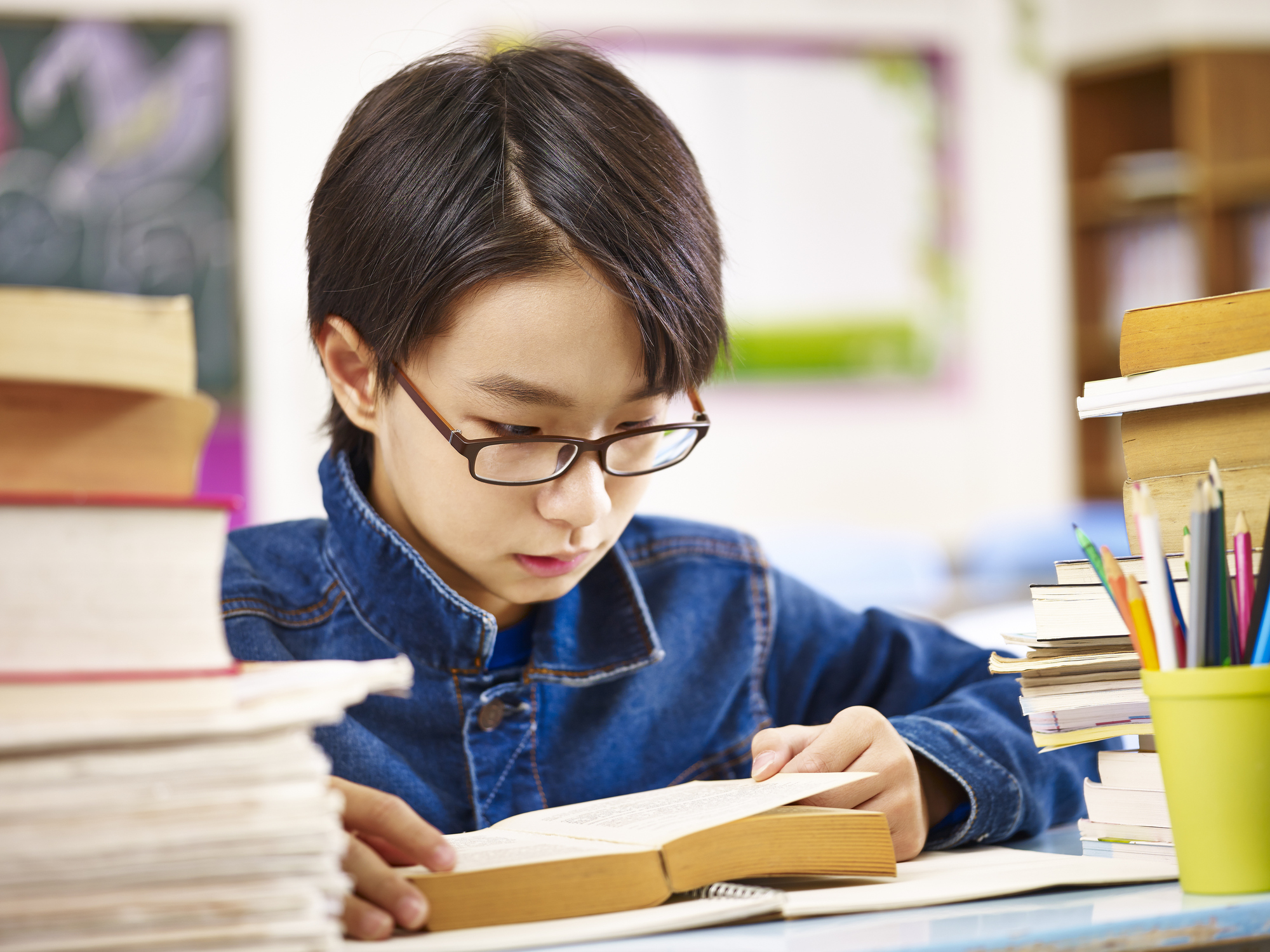 asian schoolboy reading book in classroom