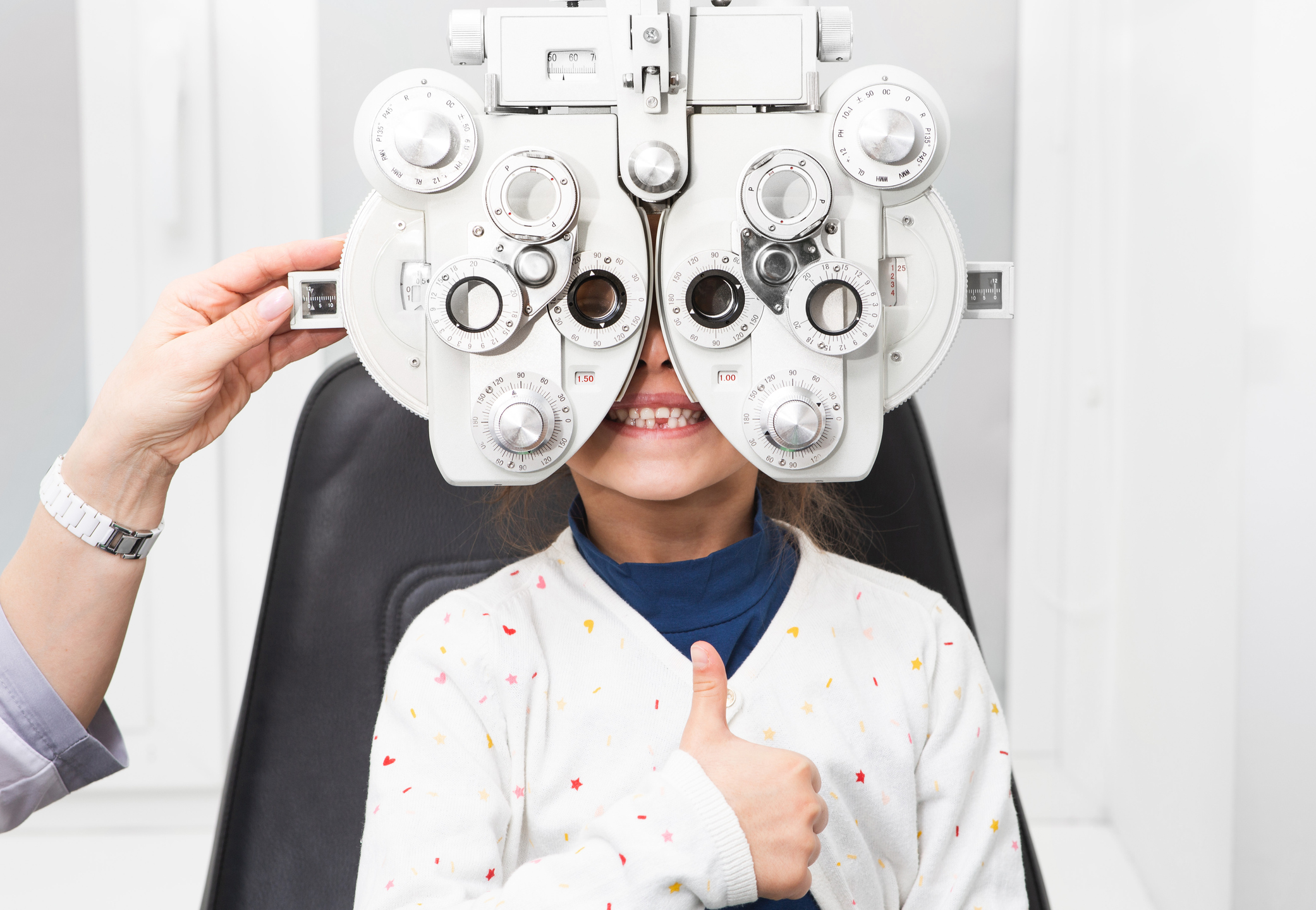 Girl shows thumb up at an ophthalmologist’s appointment. Phoropter – a device for measuring refractive error and for determining information for a prescription for glasses