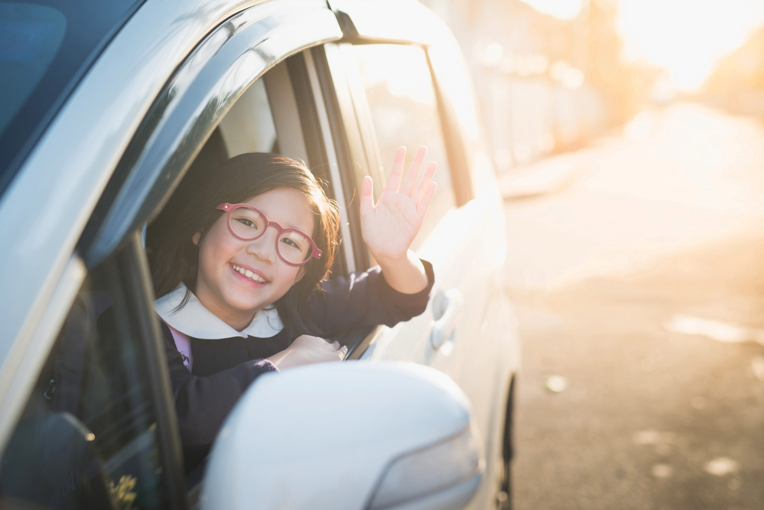Asian girl in student uniform going to school by car and  waving goodbye