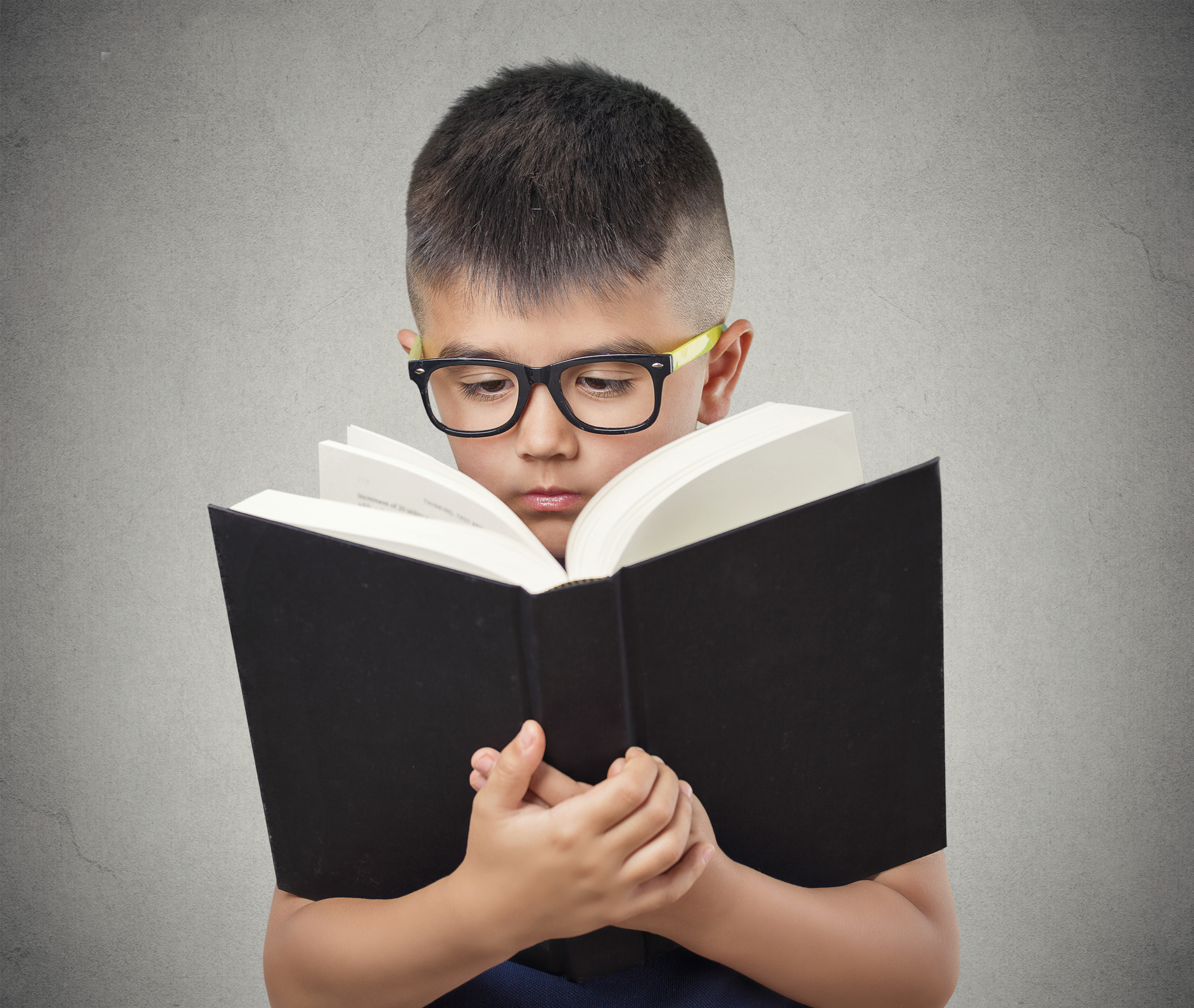 closeup portrait child boy with glasses reading holding book too close having difficulty to see text,