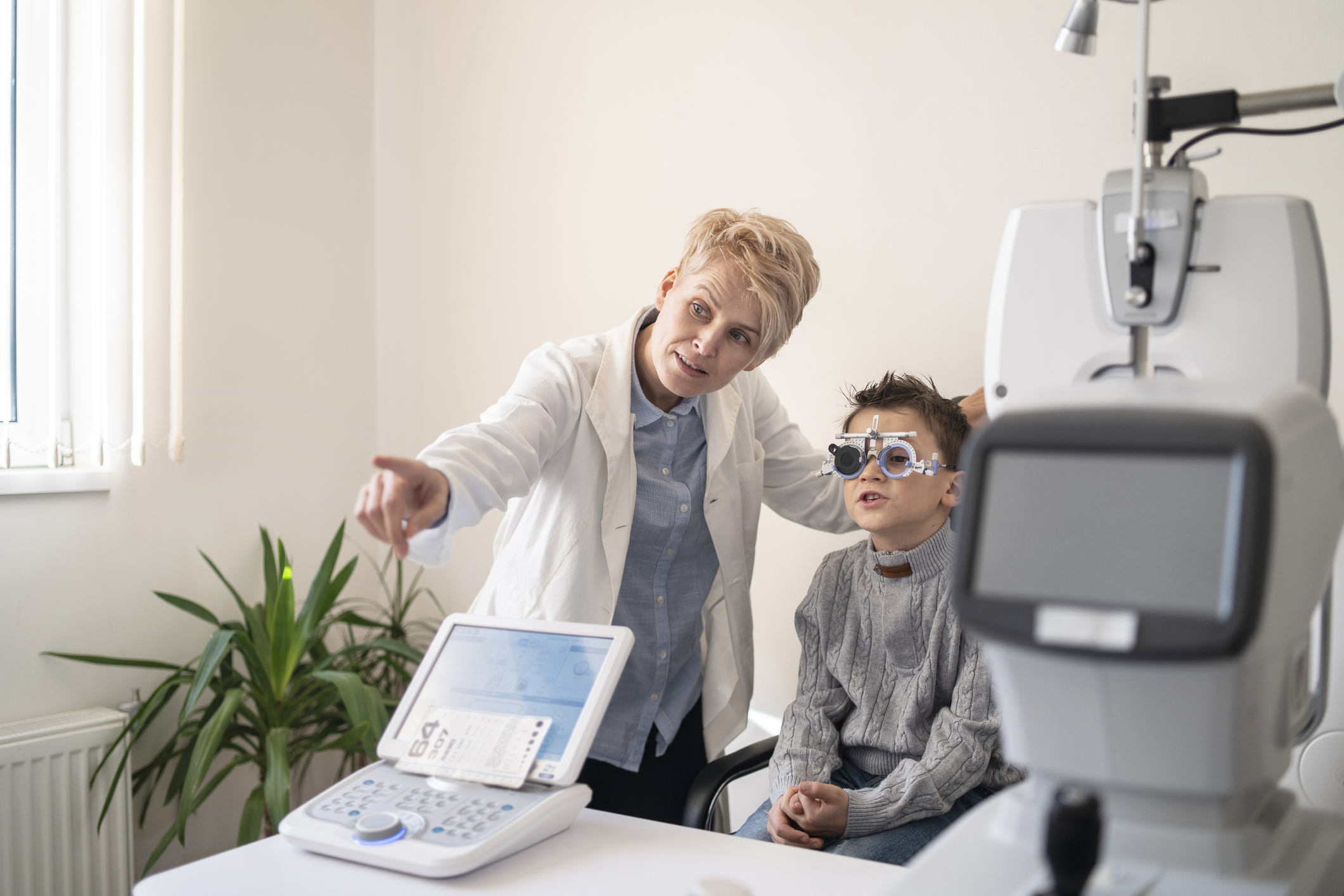 Female optometrist points to the Snellen Chart, while a young boy reads out the letters