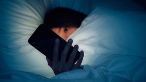 A young girl is in bed looking at her cellphone
