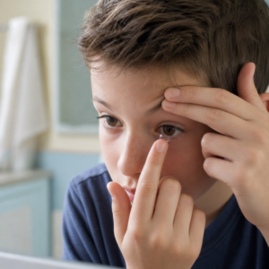 A young boy puts in a contact lens