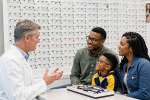 An eye doctor talks to a young patient and his parents in front of a frame board 
